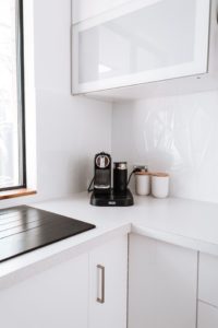 Fragment nowoczesnej, białej kuchni z ustawionym w rogu blatu ekspresem do kawy.